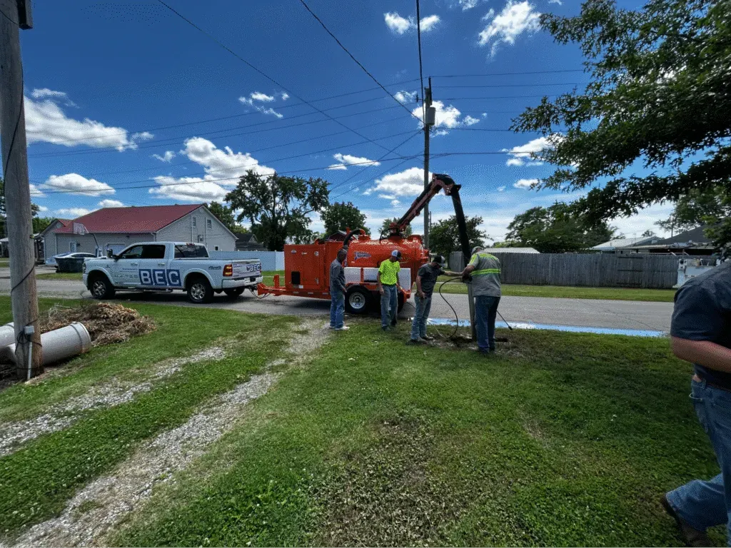 Workers operating performing narrow trench excavation for utility maintenance on a bright, sunny day.