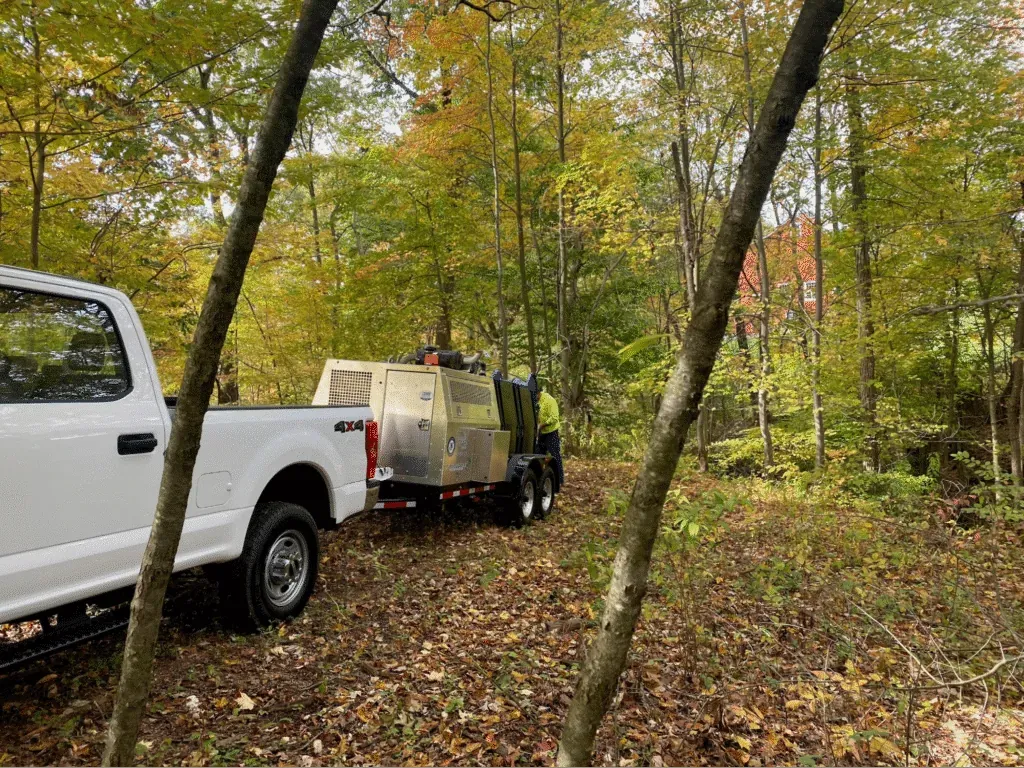 Jetter maintenance tips concept with jetter trailer parked amidst active autumn foliage in a wooded area.