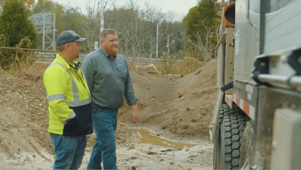 Two professionals discussing optimal control for precision mixing equipment in a construction site.
