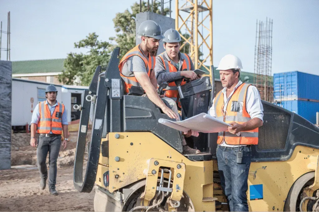 Construction workers collaborating on site, reviewing plans with safety gear and equipment.