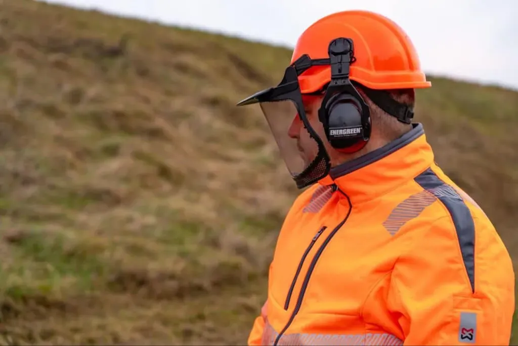Outdoor worker in safety gear, including an orange helmet and protective headphones.