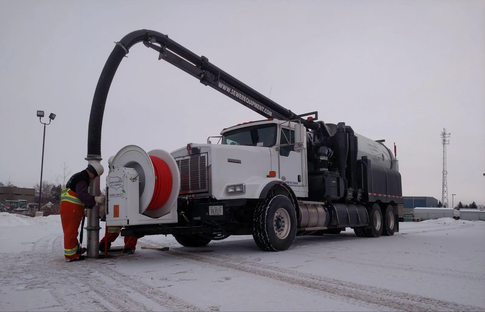Combination sewer truck operating in winter with its vacuum boom extended over a manhole.