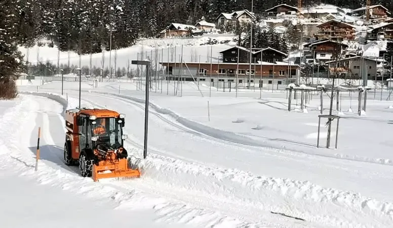 Snow plow clearing a snowy path in a winter landscape with cozy cabins.