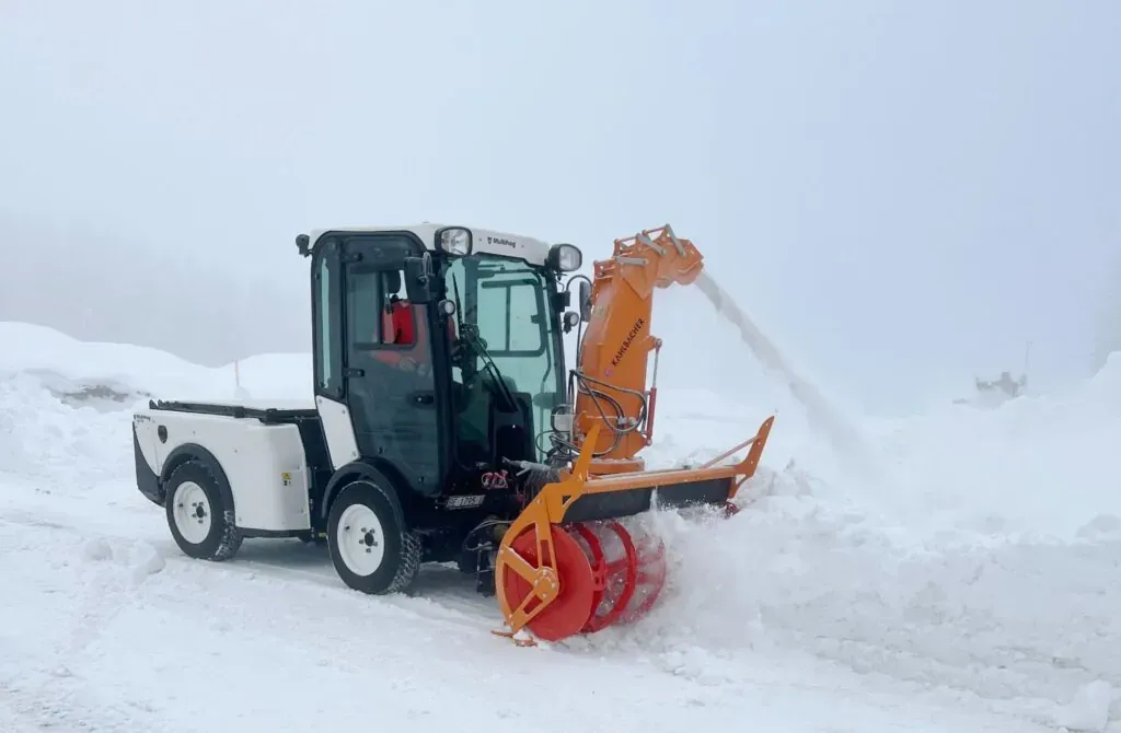 Snow plow clearing a winter road in foggy conditions.