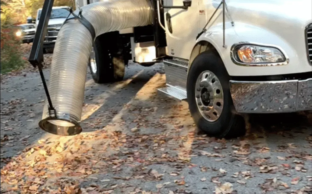 Leaf vacuum truck cleaning a gravel path covered in autumn leaves.
